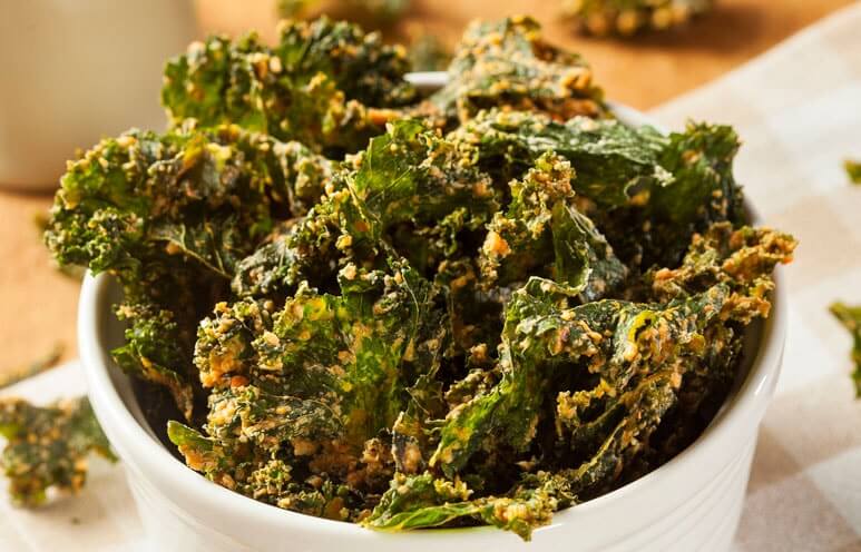 A mouthwatering bowl of kale chips seasoned with what appears to be nutritional yeast.