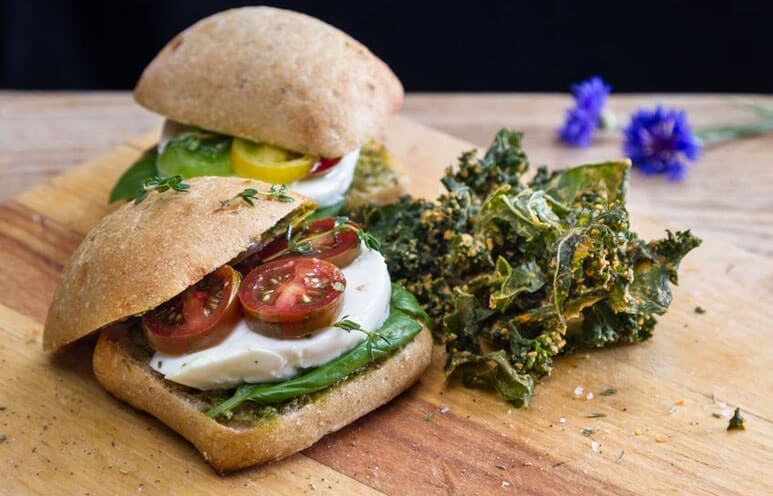 Seasoned kale chips placed beside a vegetarian slider on a cutting board.